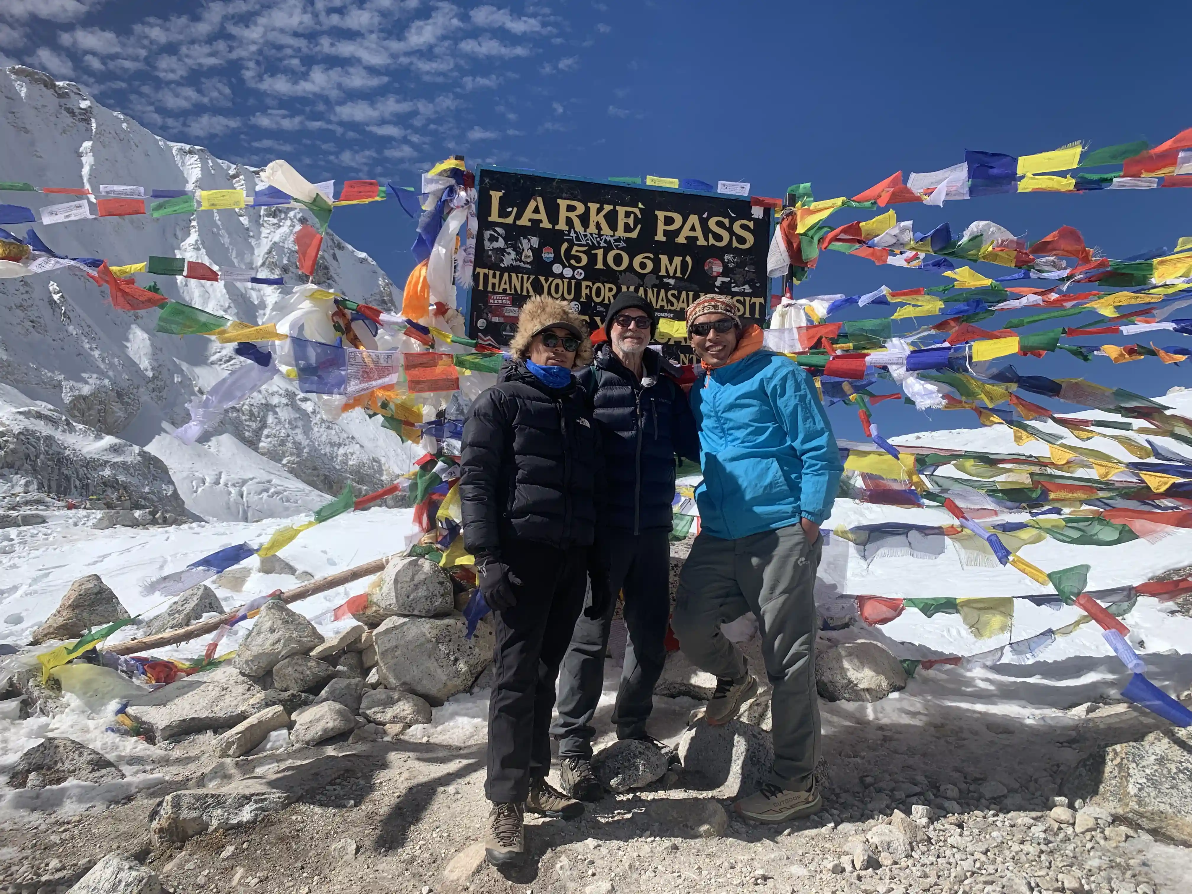 Trekkers at Larke Pass surrounded by prayer flags and snow-covered peaks